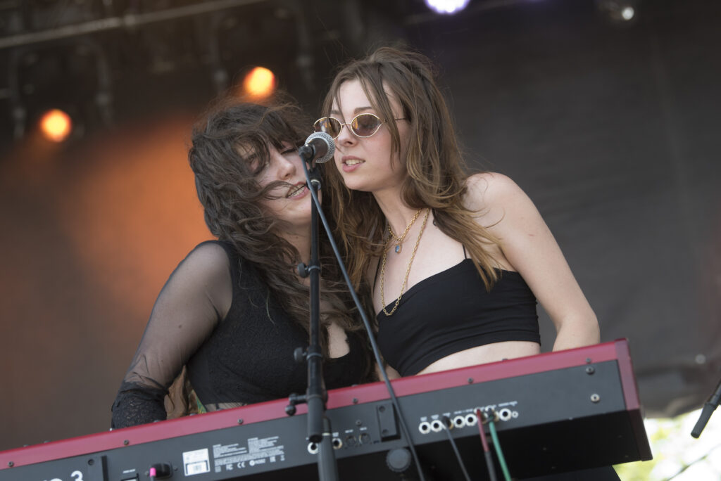 Two members of Hotel Fiction lean over a keyboard and sing into a microphone together.